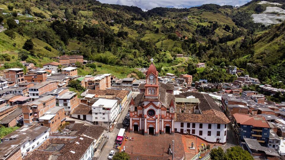A town with a prominent church featuring a clock tower, surrounded by hilly terrain and residential buildings.