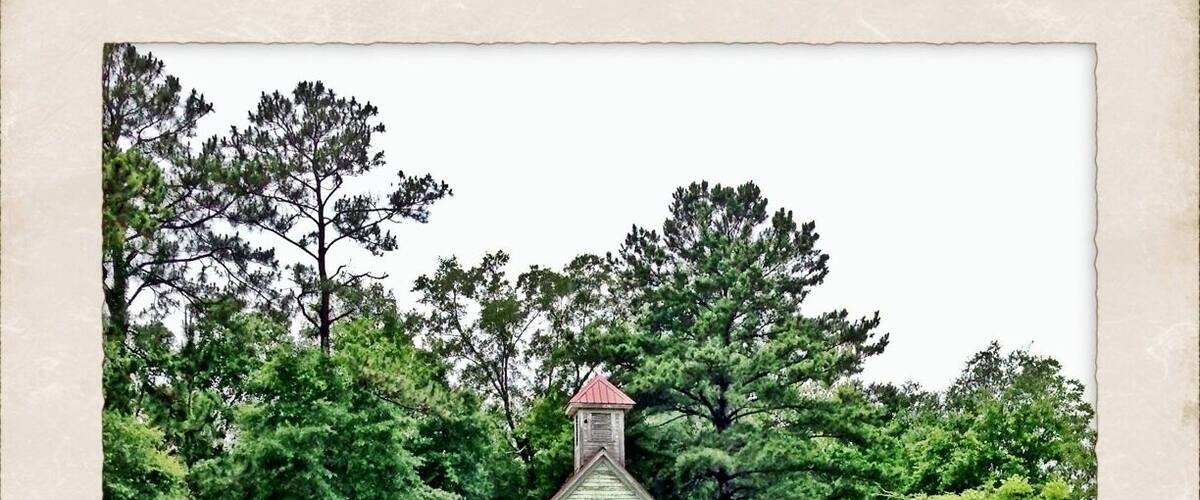 An old wooden church surrounded by lush green trees and grass.