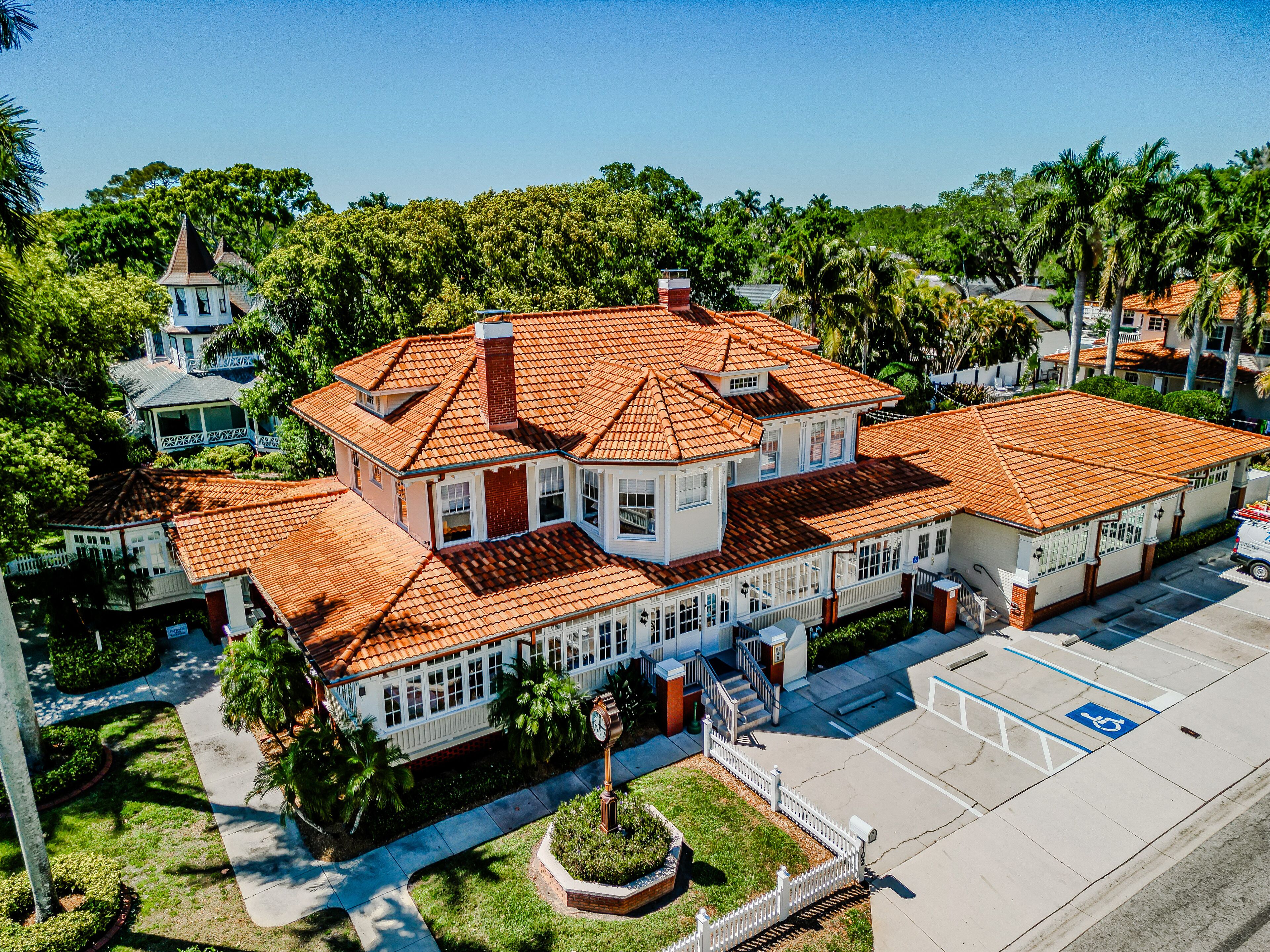 A large, multi-story building with a red-tiled roof, surrounded by lush greenery and palm trees.