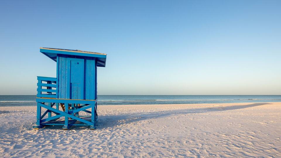 Een blauwe redderstoere op een zandstrand, met de oceaan op de achtergrond.