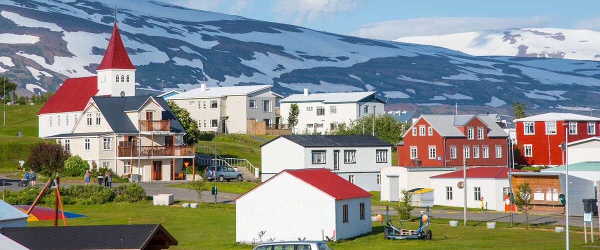 A town with a church, red-roofed houses, and a snow-capped mountain in the background.