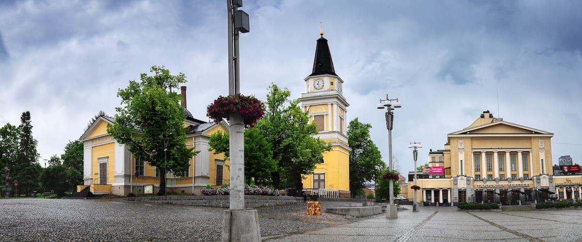 A historic building with a clock tower, surrounded by trees and a cobblestone plaza.