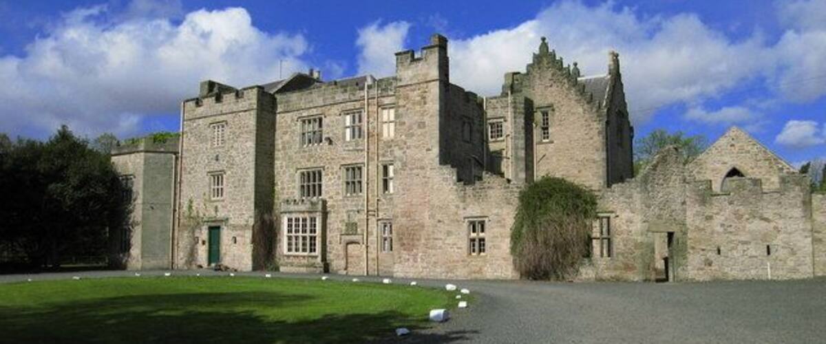 A historic stone castle with a large lawn in front.