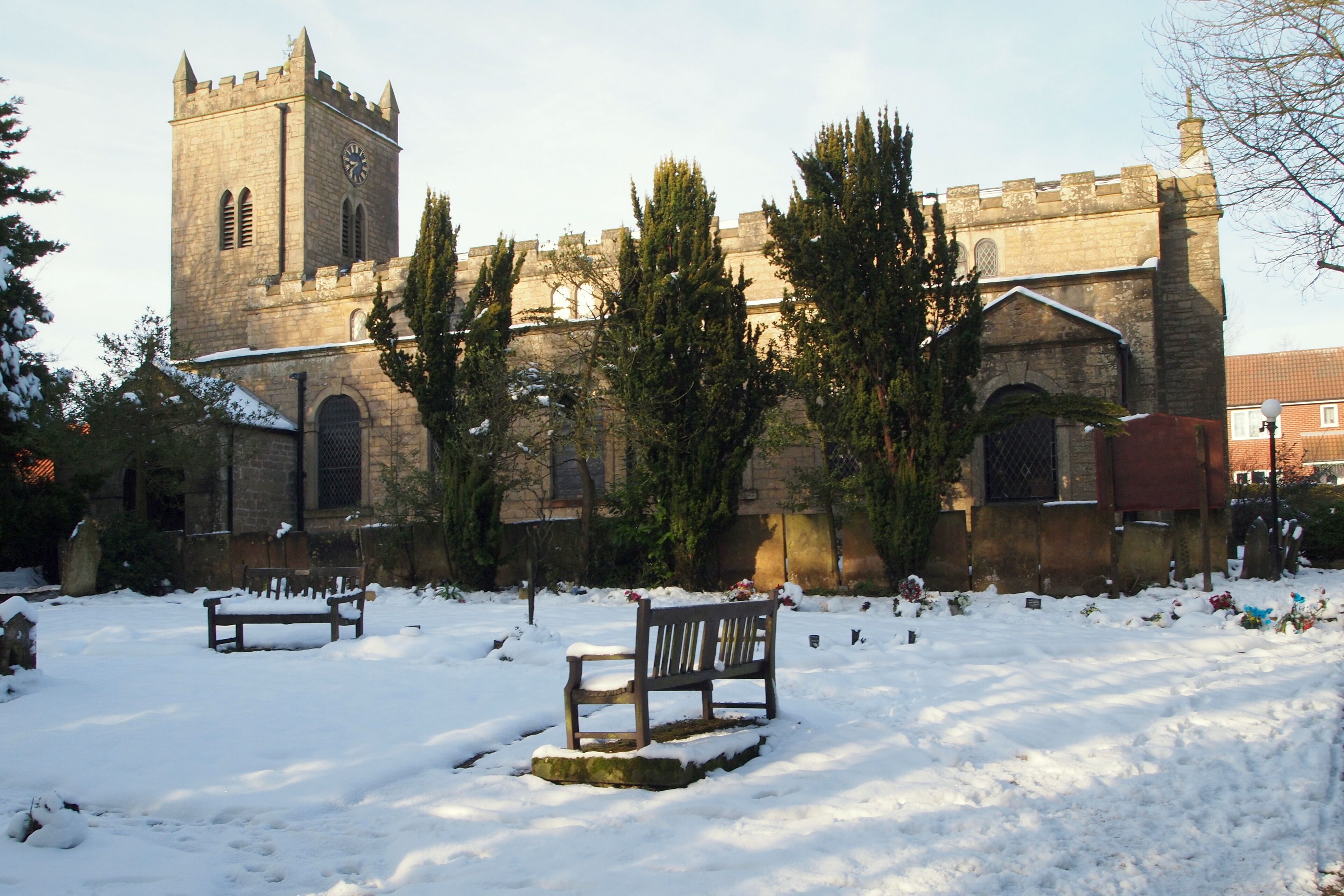 A snow-covered church with a tall tower and a bench in the foreground.