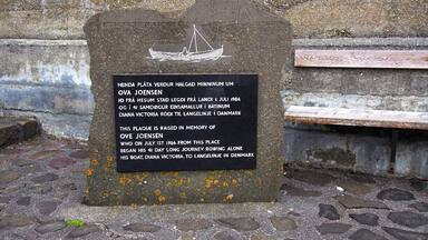 A memorial plaque with a boat illustration and text commemorating Ove Jensen's 1986 rowing journey from this location to Denmark.