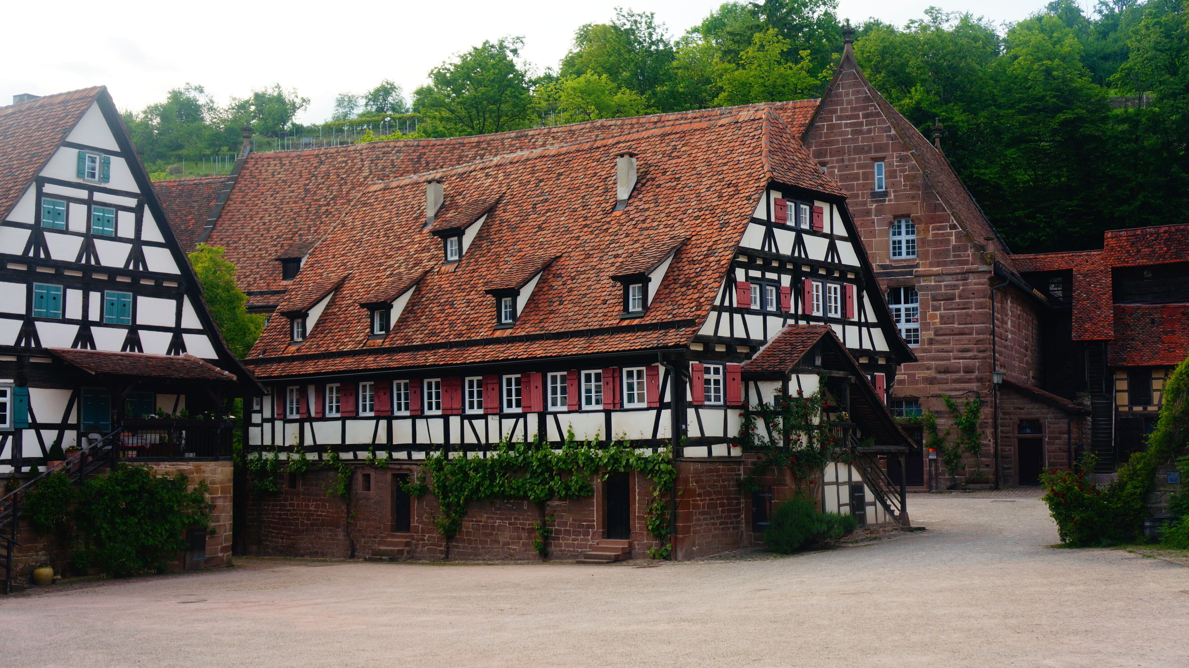 A traditional half-timbered house with a steeply pitched roof, surrounded by lush greenery.