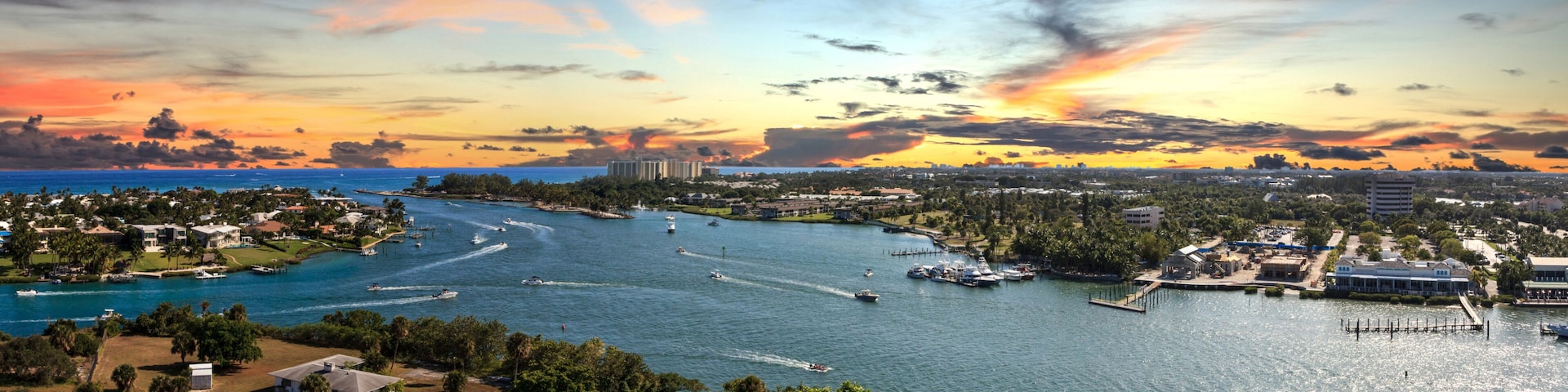 Un paisaje urbano costero con un puerto deportivo, barcos y un cielo al atardecer.