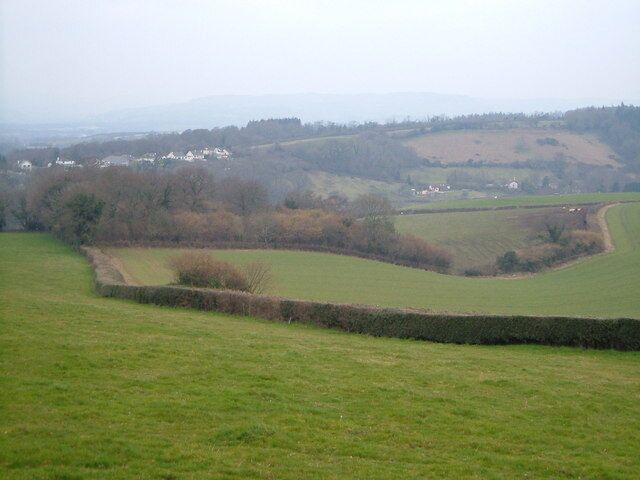 A rural landscape with rolling hills, a stone wall, and scattered houses in the distance.