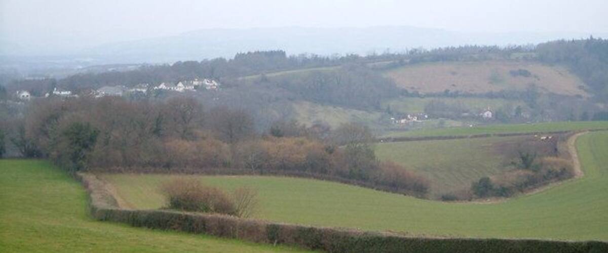 A rural landscape with rolling hills, a stone wall, and scattered houses in the distance.