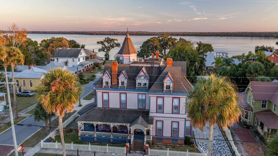 A historic house with a distinctive tower, surrounded by palm trees and a waterfront view.