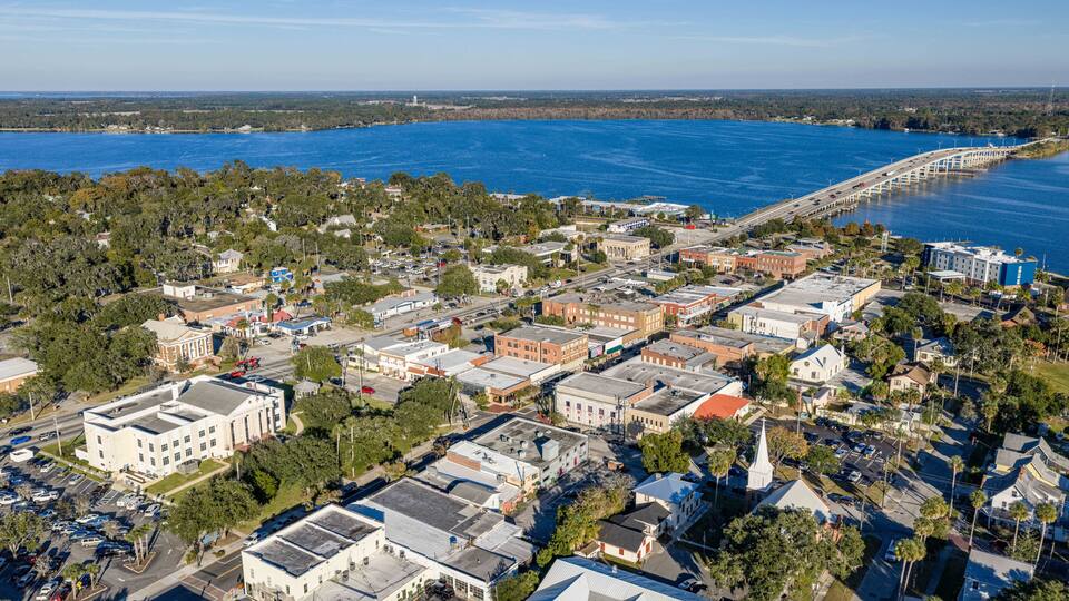 An aerial view of a coastal town with a bridge, buildings, and a large body of water.