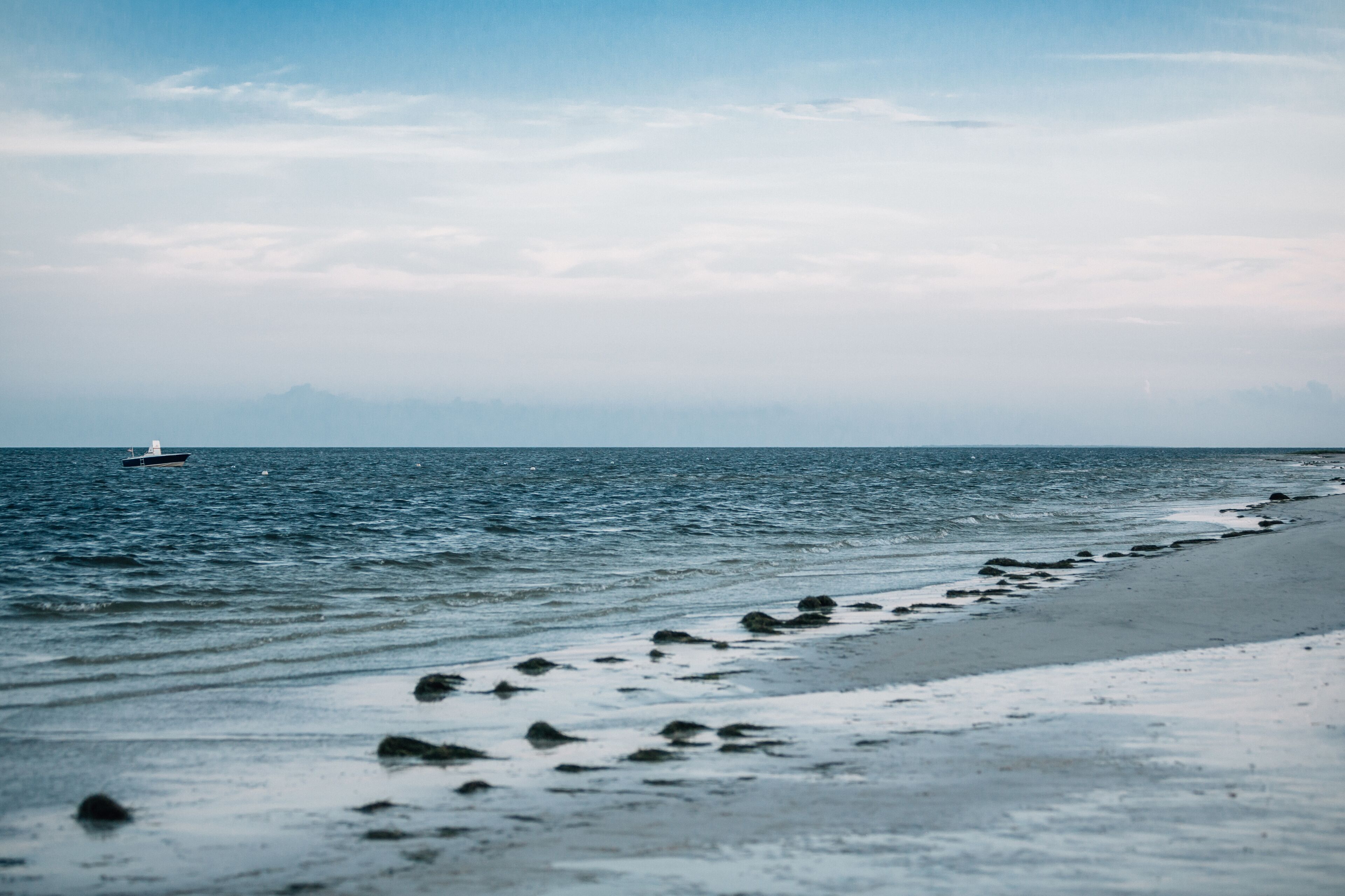 A beach with a boat in the water and a rocky shoreline.
