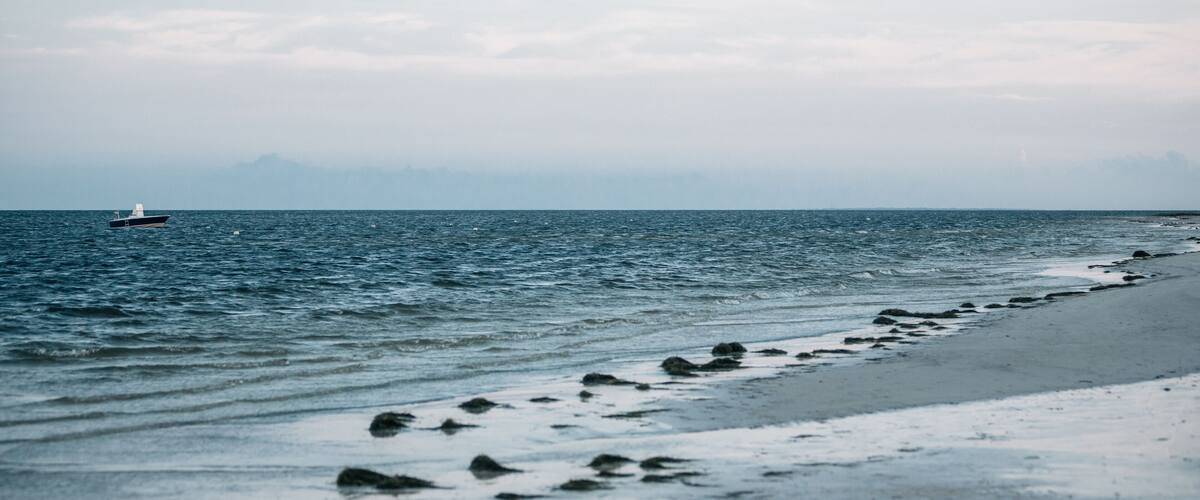 A beach with a boat in the water and a rocky shoreline.