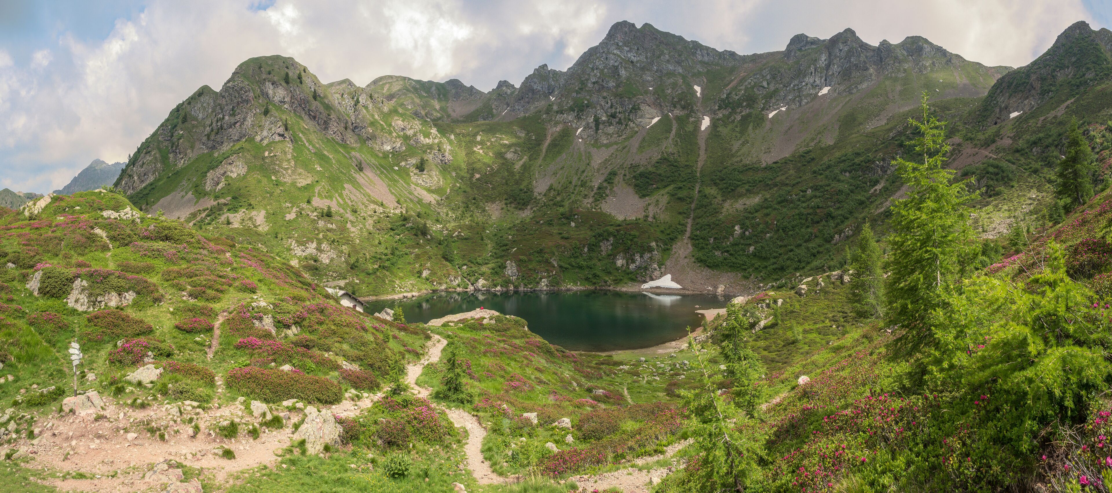 A mountainous landscape with a lake surrounded by green hills and rocky peaks.