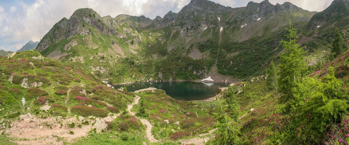 A mountainous landscape with a lake surrounded by green hills and rocky peaks.