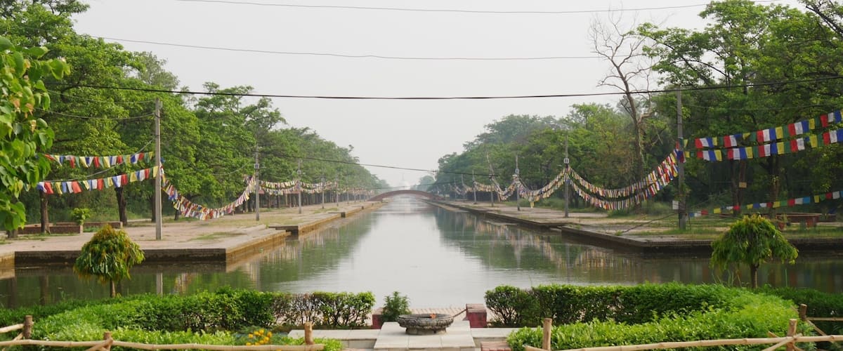 A canal flanked by trees and decorated with colorful prayer flags.