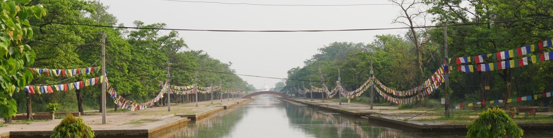 A canal flanked by trees and decorated with colorful prayer flags.