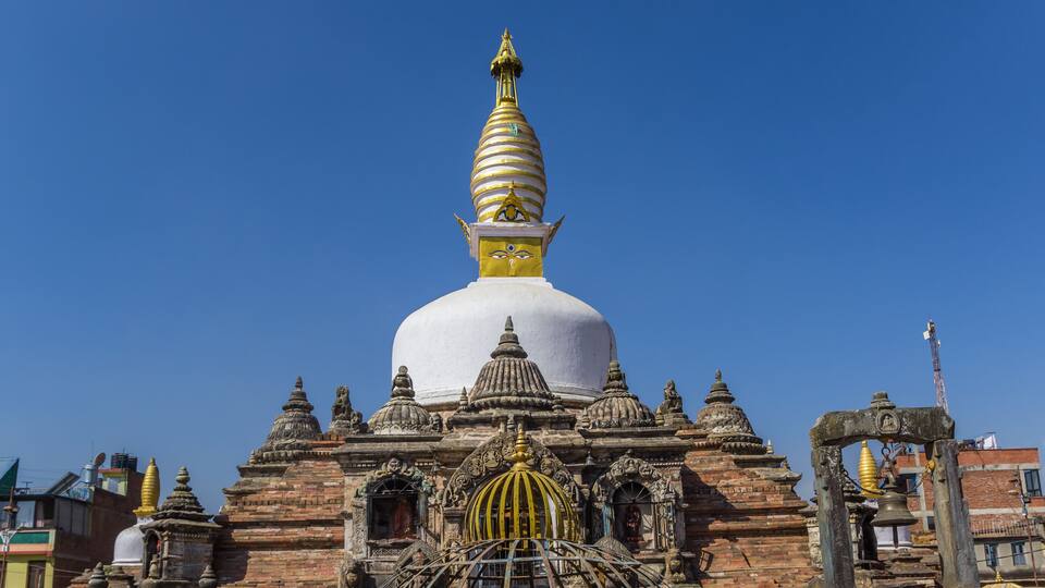 A large white stupa with a golden spire, surrounded by intricate brick architecture and smaller domes.