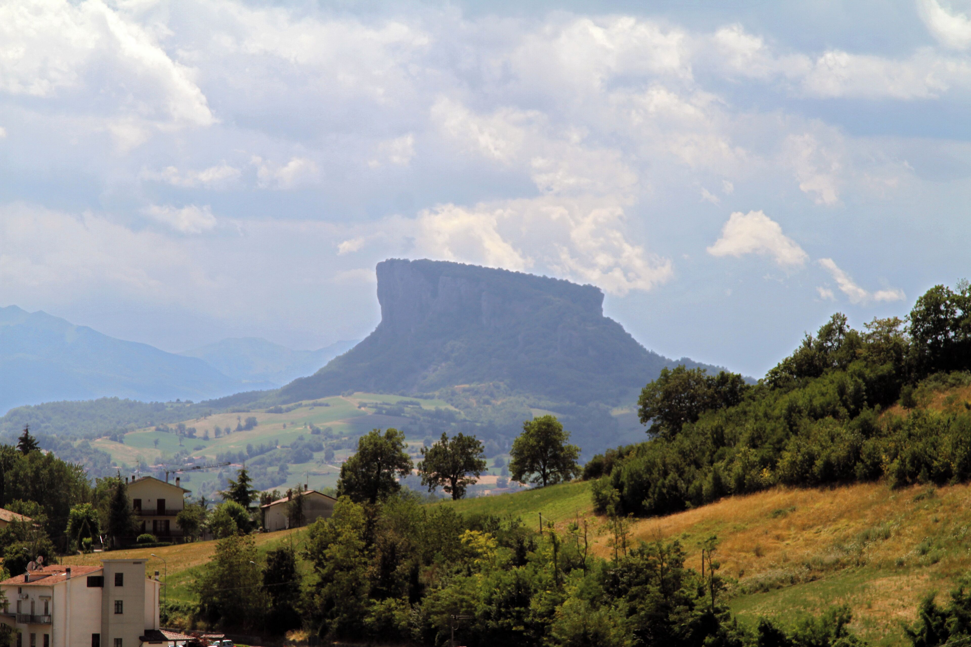 A mountainous landscape with a prominent rock formation, green hills, and scattered buildings.