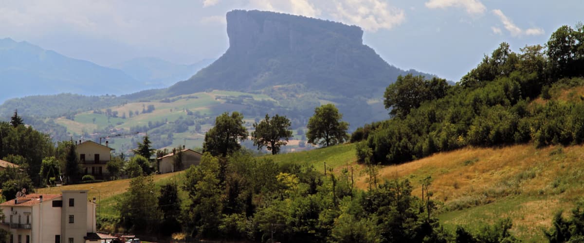 A mountainous landscape with a prominent rock formation, green hills, and scattered buildings.