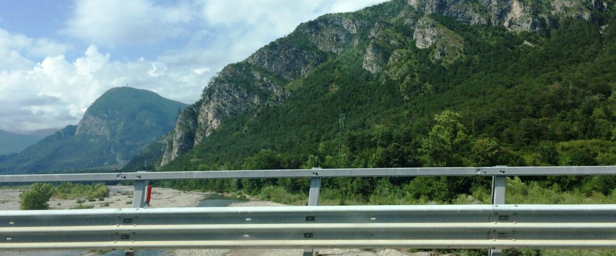A mountainous landscape with a river and a guardrail in the foreground.