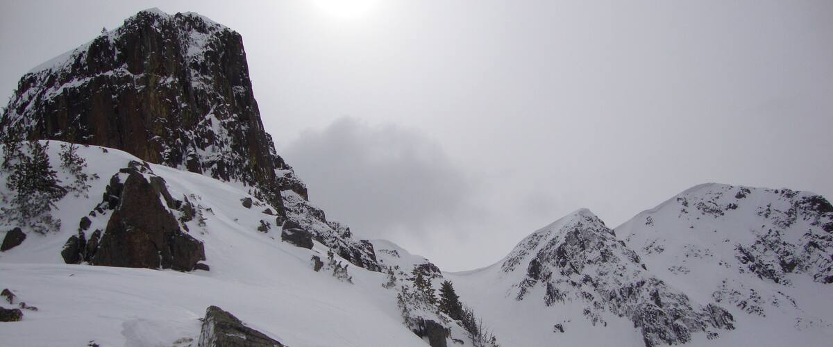 A snow-covered mountain range with rocky outcrops and a bright sun in the sky.