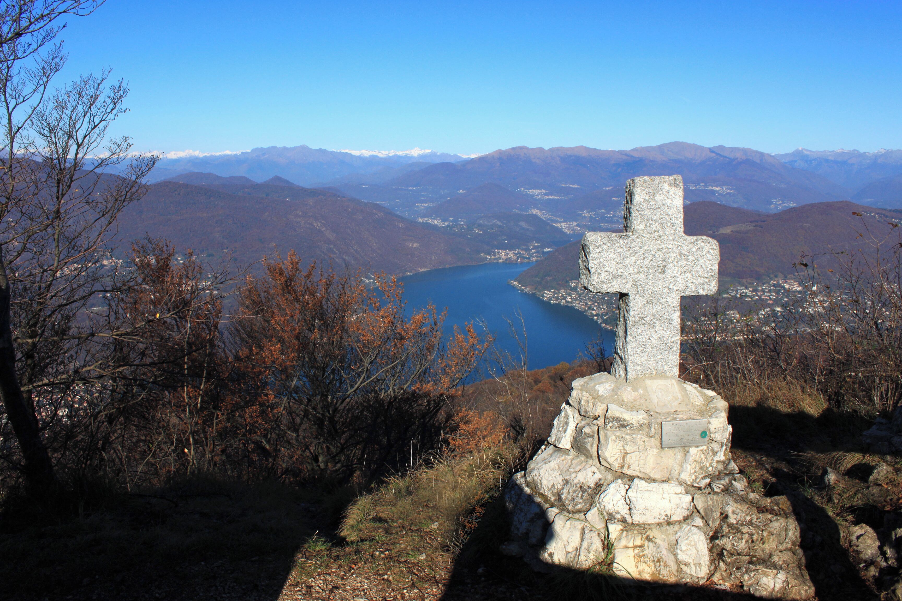 A stone cross on a hill overlooking a lake and mountains.