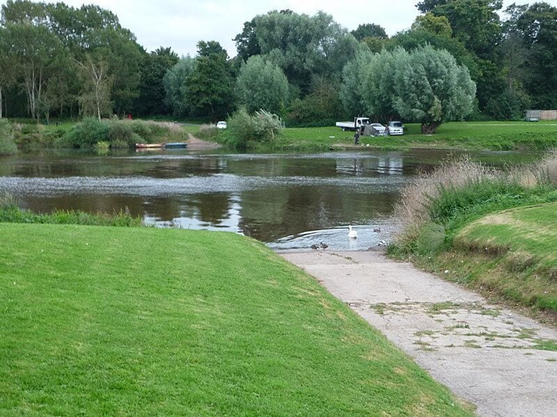 A river with a boat, grassy banks, trees, and a path.