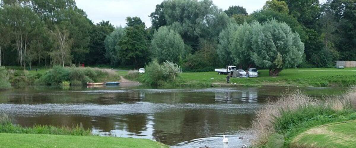 A river with a boat, grassy banks, trees, and a path.