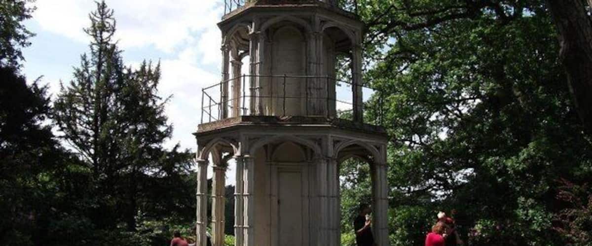 A historical tower with a clock, surrounded by trees and a pathway.