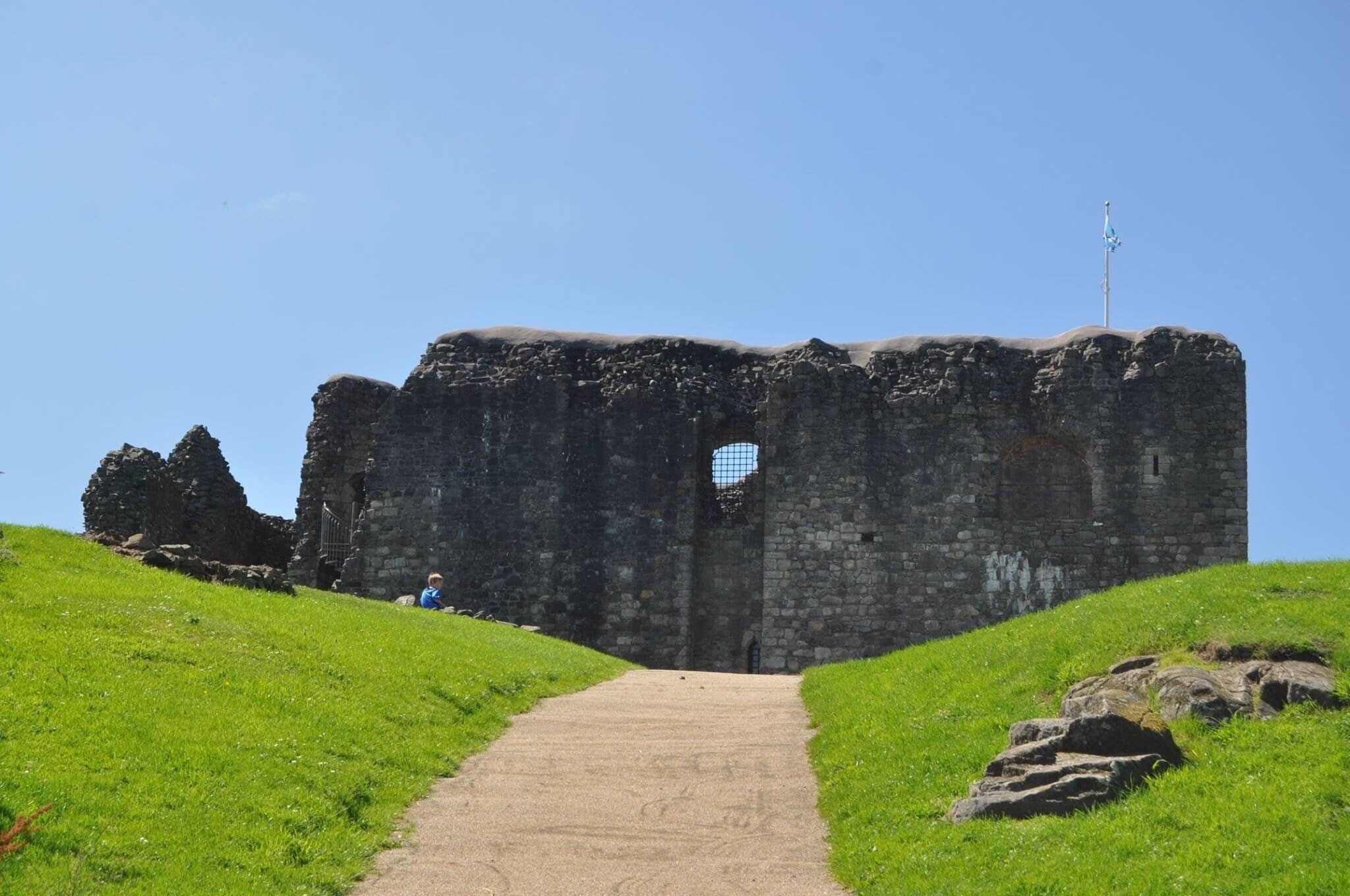 A stone castle ruin with a clear sky, a pathway leading to the entrance, and a weather vane on top.