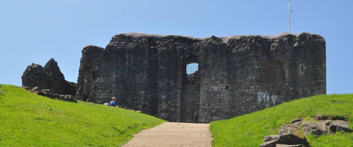 A stone castle ruin with a clear sky, a pathway leading to the entrance, and a weather vane on top.