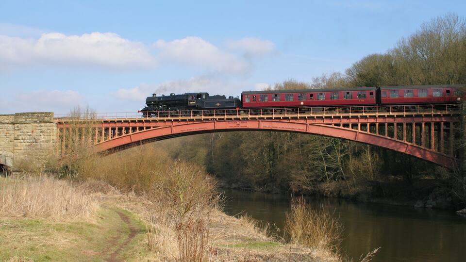 A train crossing a stone bridge over a river.