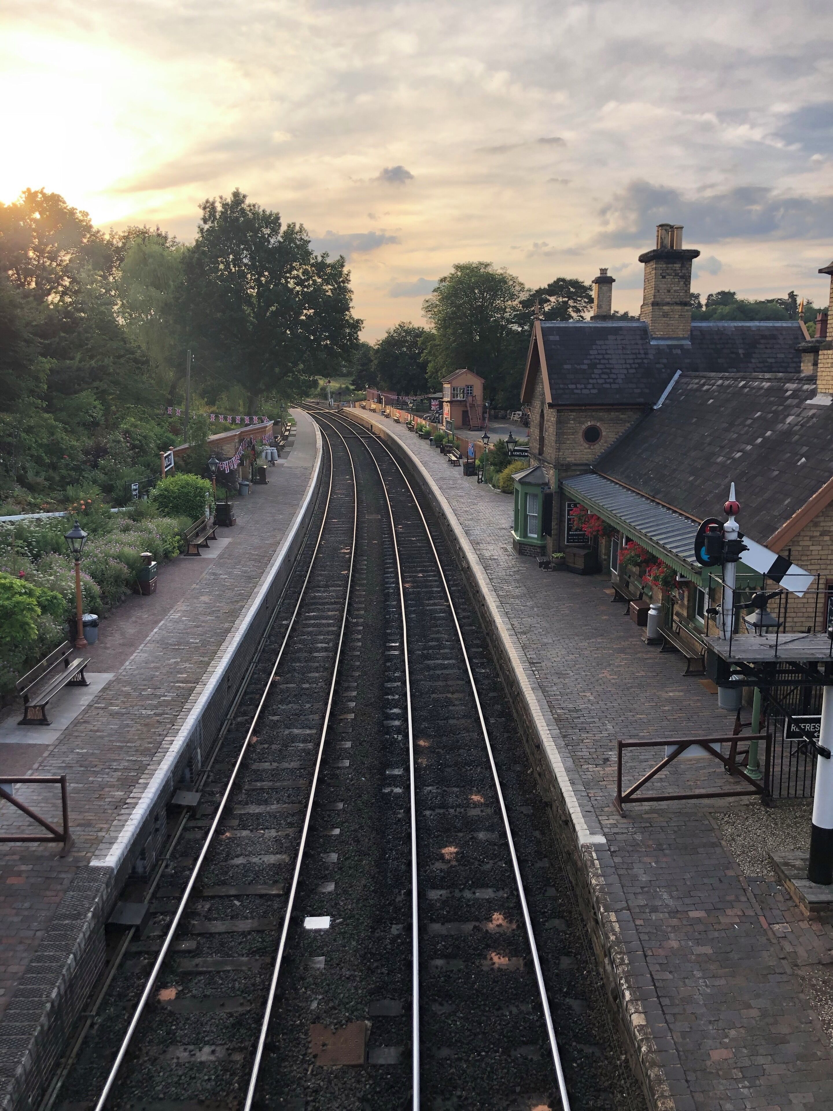 A railway station with two tracks, a platform, and a small building with a clock.