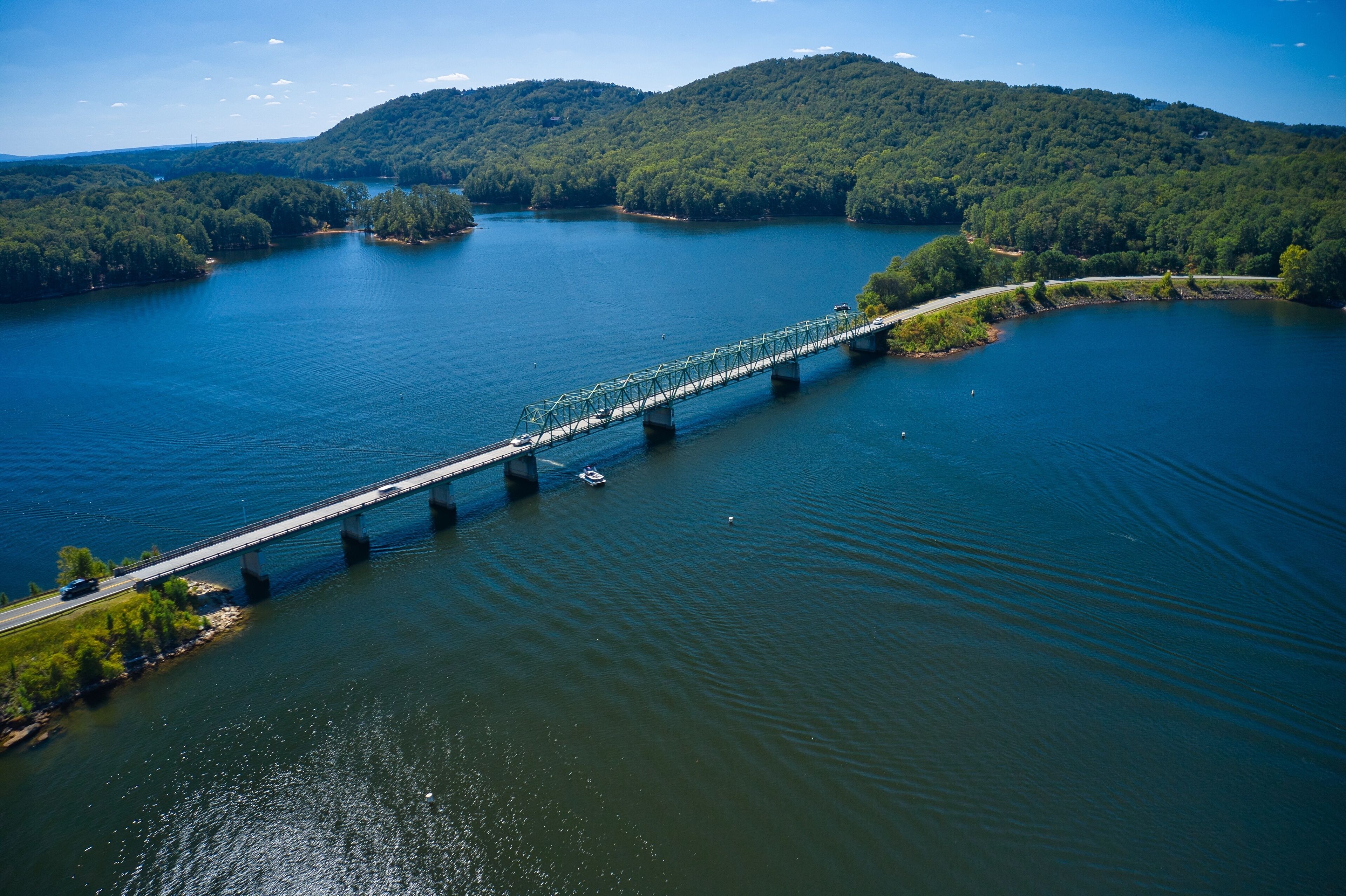 A bridge over a large body of water with forested hills in the background.