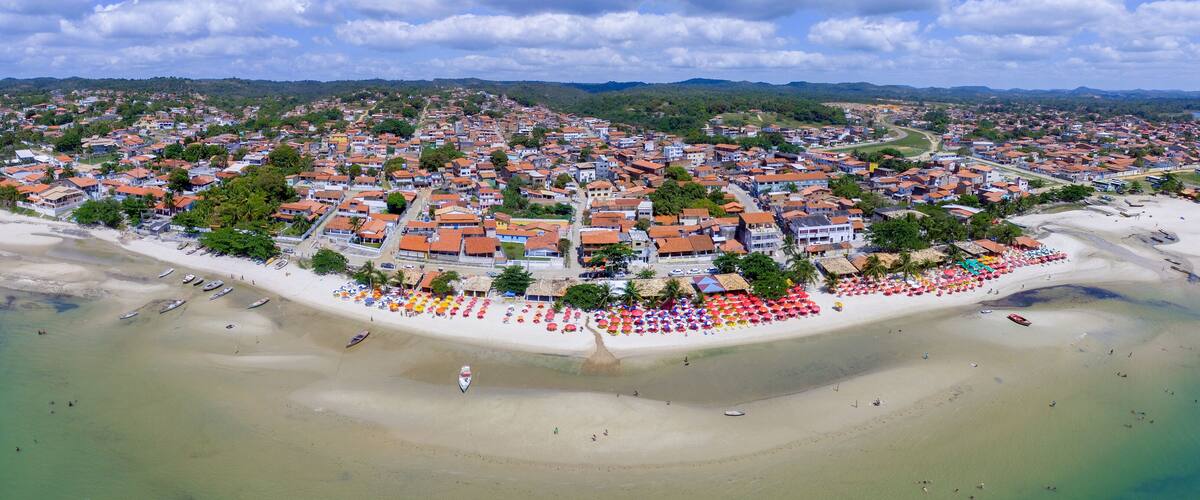 An aerial view of a coastal town with a beach, houses, and a hilly landscape in the background.
