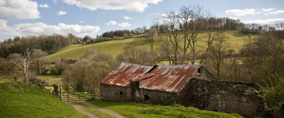 A rural landscape with a stone barn, a dirt path, and rolling hills.