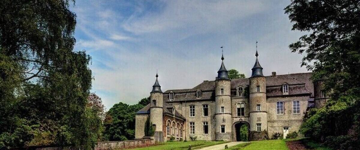A large, historic building with two towers, surrounded by a well-maintained garden and a cobblestone path.
