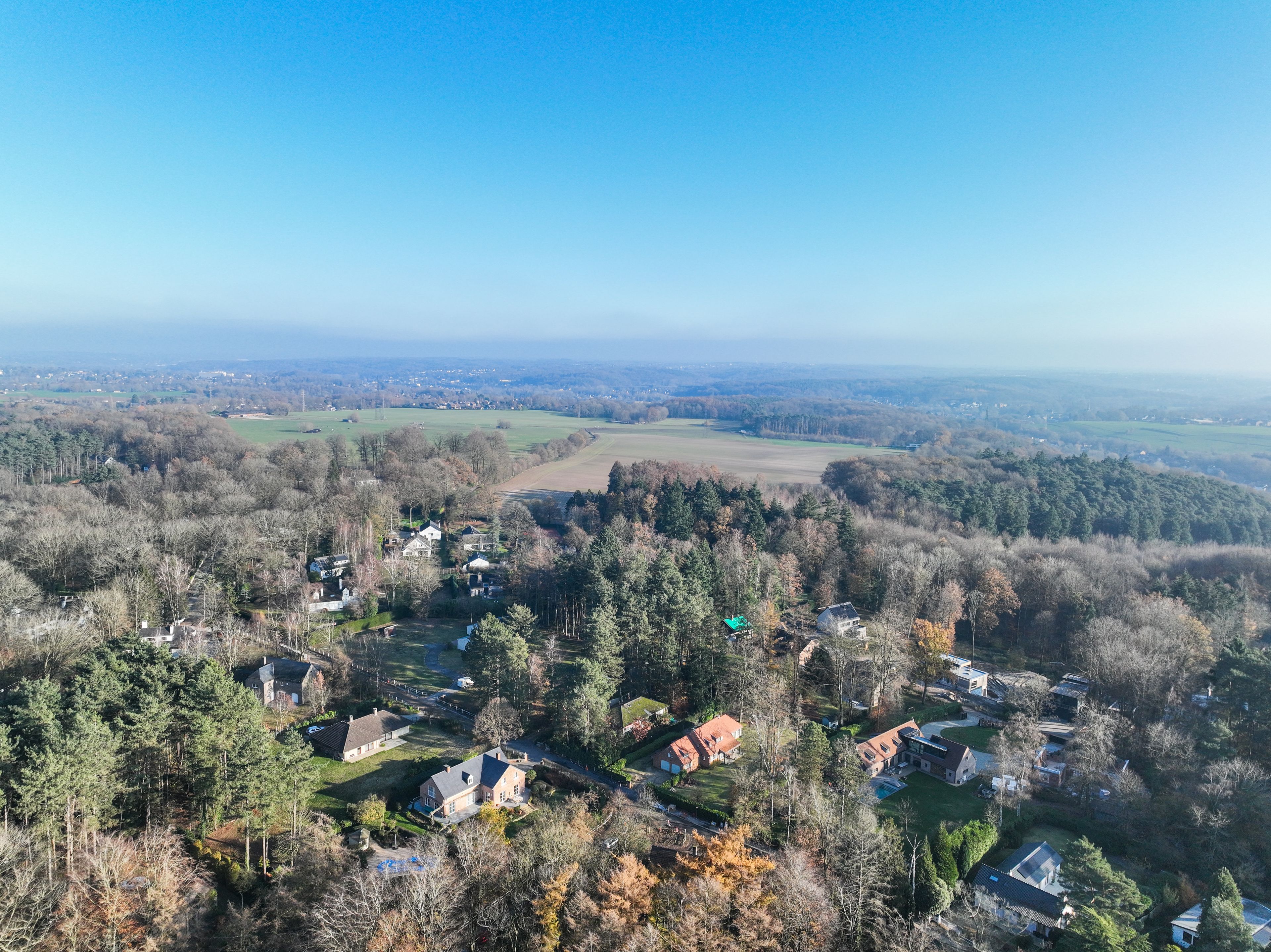 Een landelijk landschap met verspreide huizen, dichte bossen en open velden onder een heldere lucht.