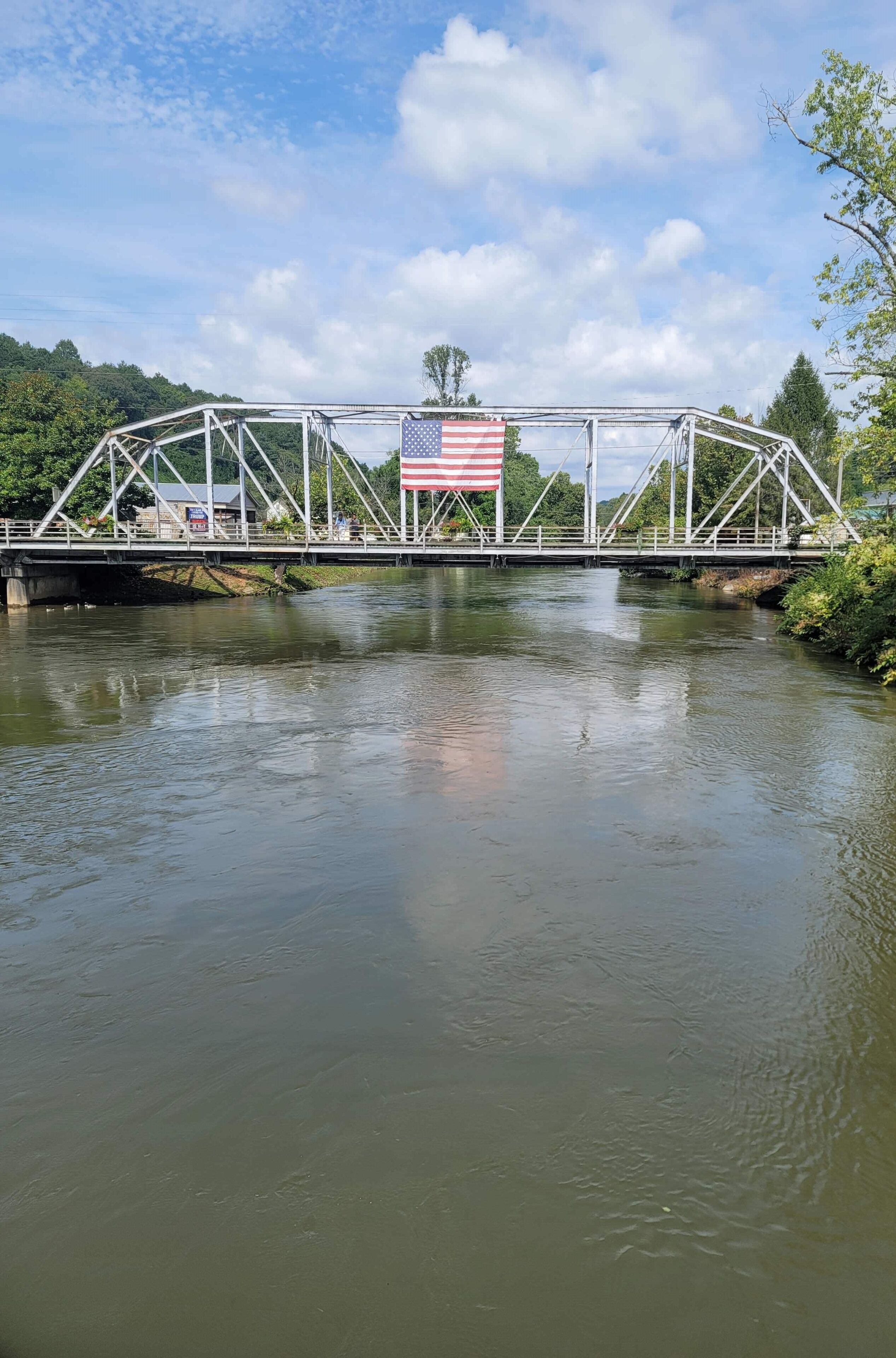 A bridge with an American flag, a river, and greenery in the background.