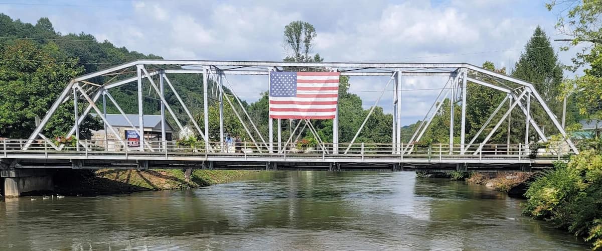 A bridge with an American flag, a river, and greenery in the background.