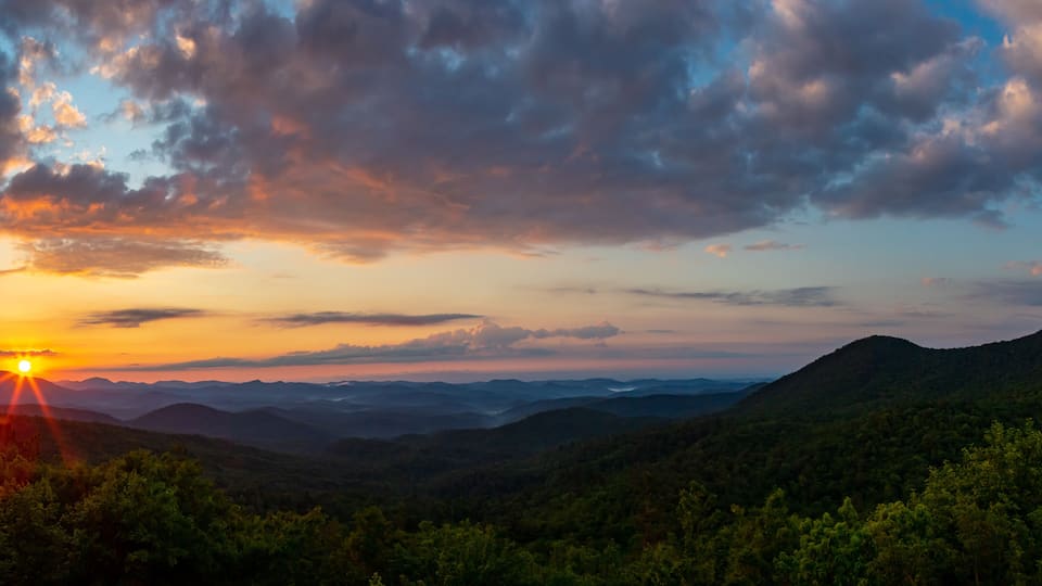 A sunset over a mountainous landscape with dense forests.
