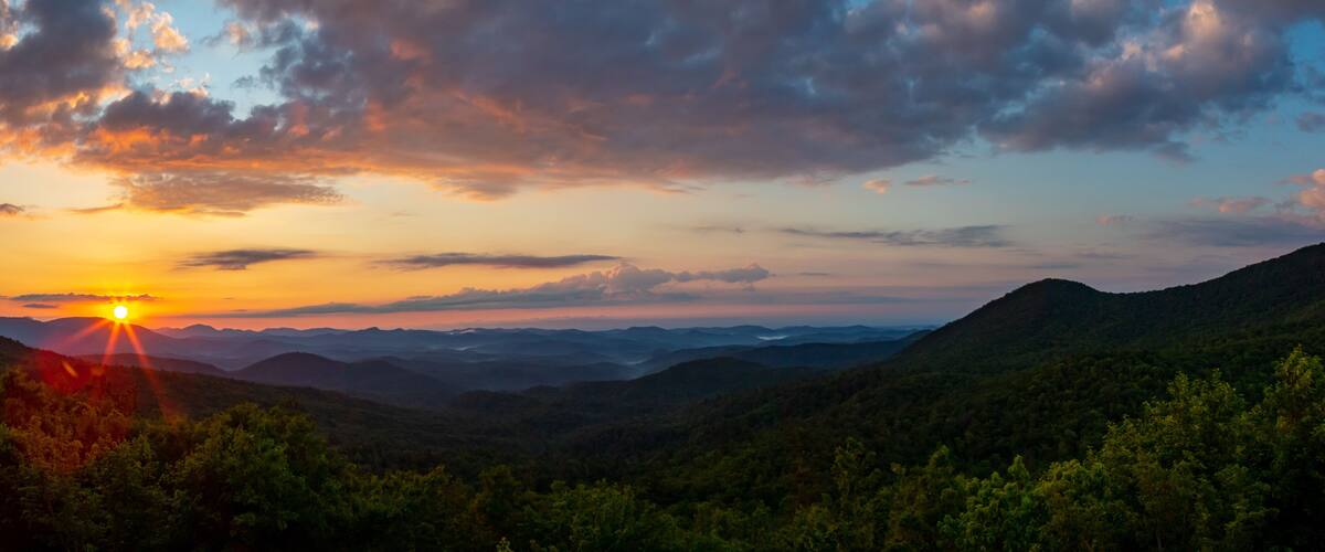 A sunset over a mountainous landscape with dense forests.