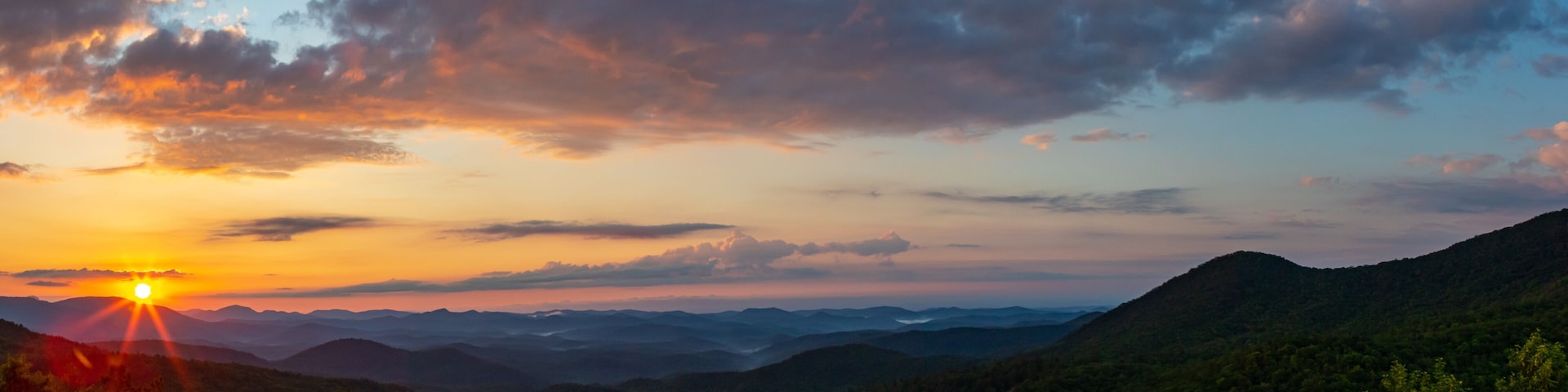 A sunset over a mountainous landscape with dense forests.