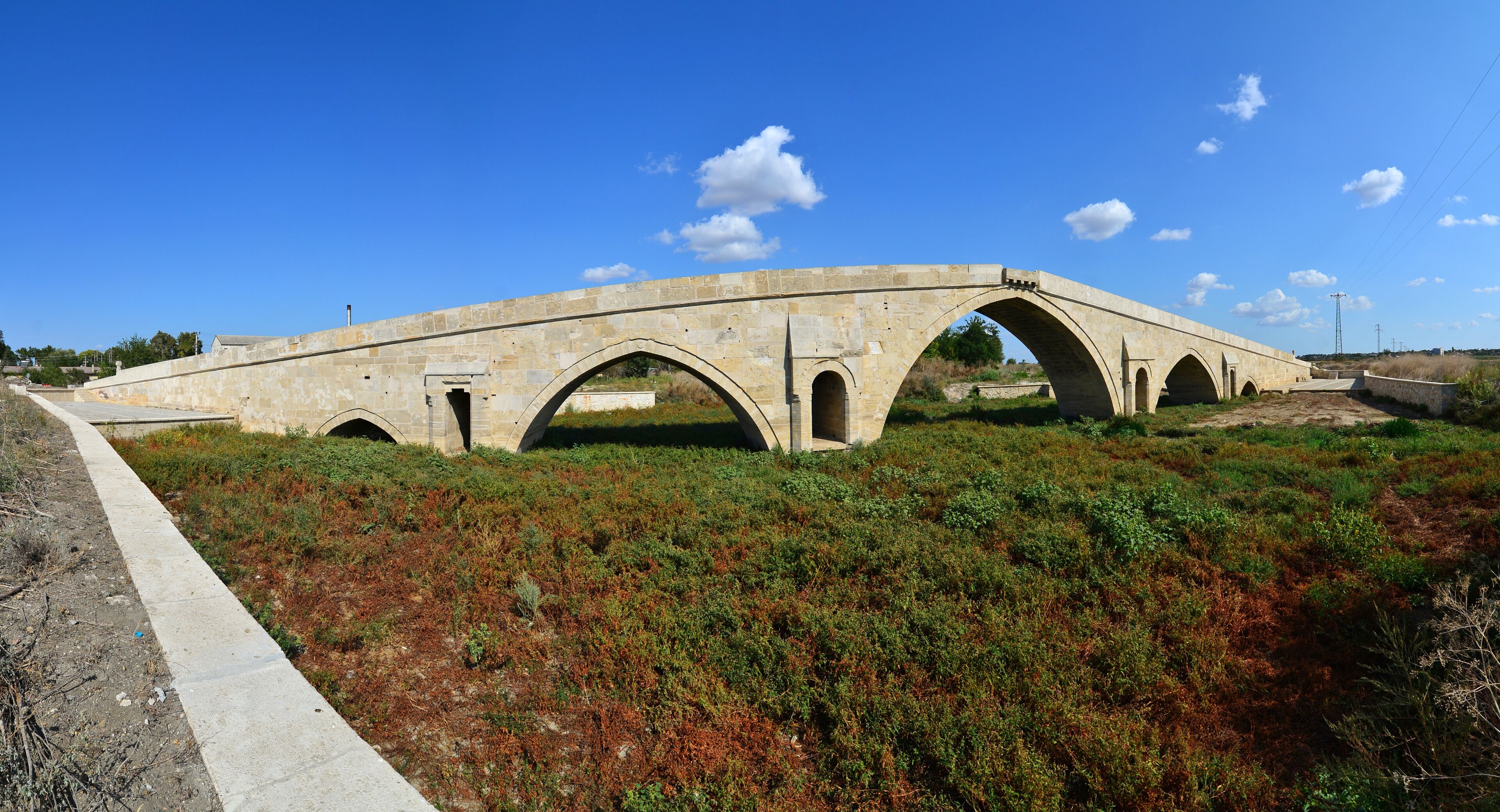 An old stone bridge with multiple arches over a grassy area.