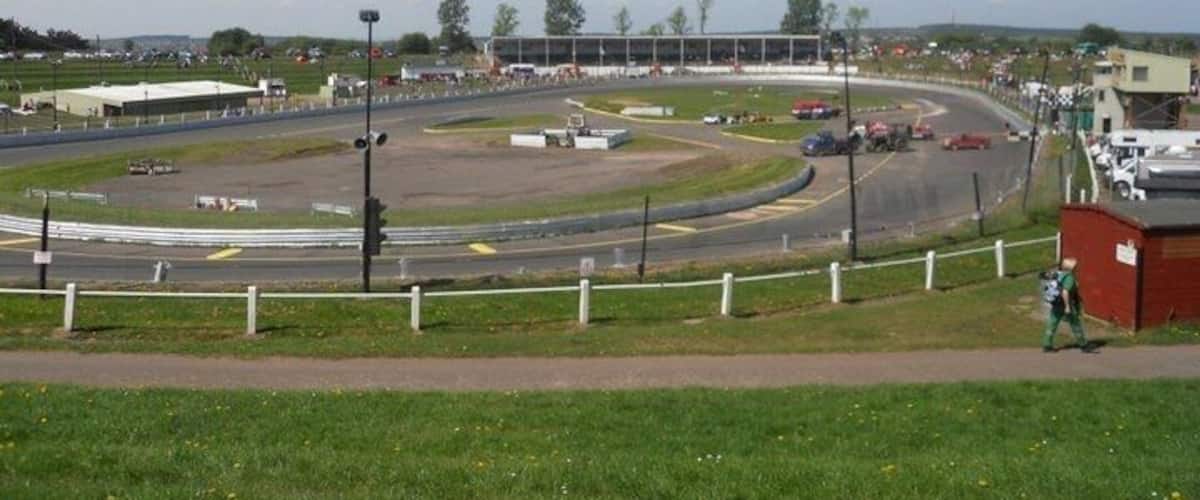 A race track with multiple lanes, spectator stands, and a grassy area with a fence.