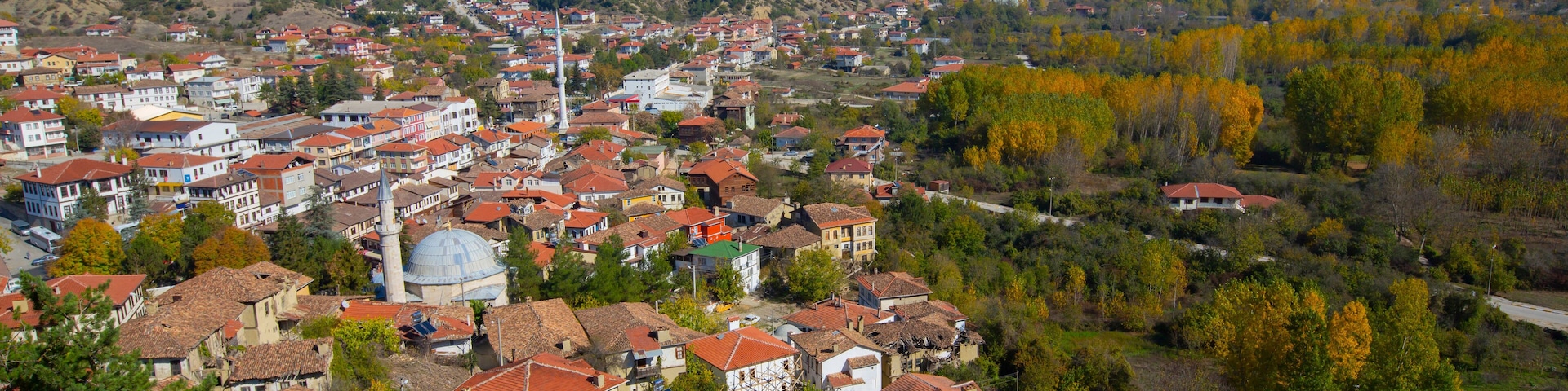 Un pueblo con casas de tejados rojos, una mezquita destacada y colinas circundantes.
