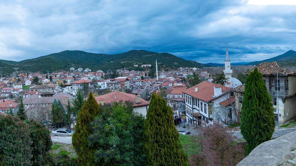 Une ville aux bâtiments aux toits rouges, avec une église blanche imposante dotée d’un clocher élancé, le tout entouré de collines verdoyantes.