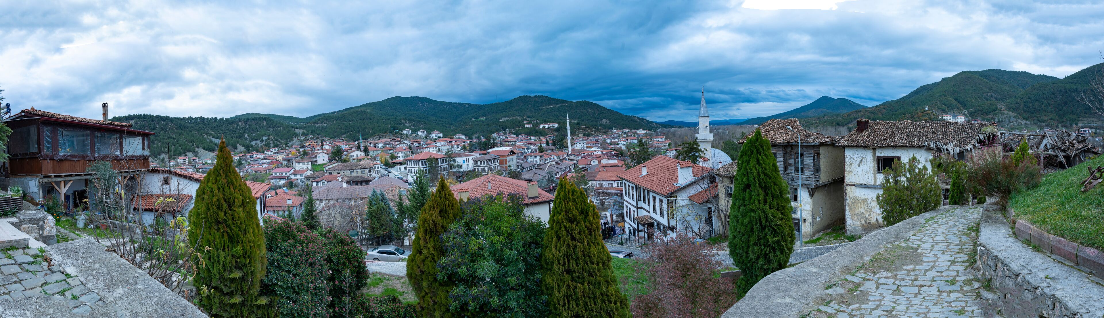 A town with red-roofed buildings, a prominent white church with a tall spire, and surrounding green hills.