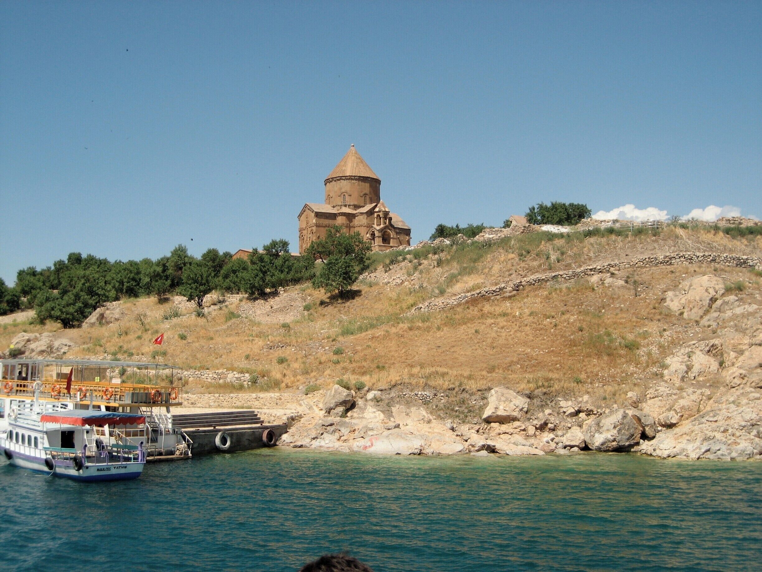 A boat docked near a rocky shoreline with a church on a hill in the background.